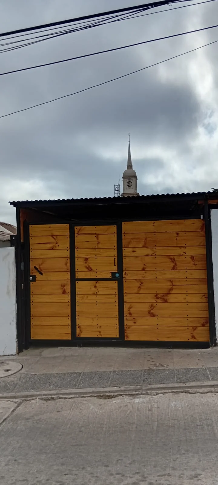 Portón frontal de metal negro y revestimiento de madera con puerta peatonal integrada