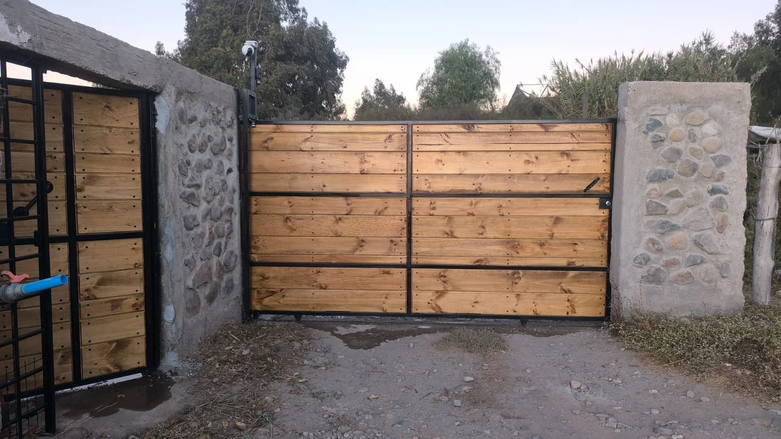 Portón de estructura metálica y madera instalado entre pilares de piedra